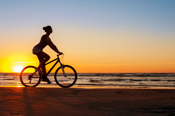 Fototapeta na wymiar Silhouette of sporty woman riding bicycle on multicolored sunset