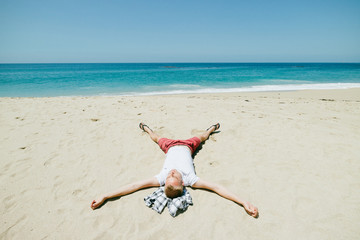 Man relaxing on beautiful empty white sand beach with clear blue water along the Pacific Coast Highway Route 1, California
