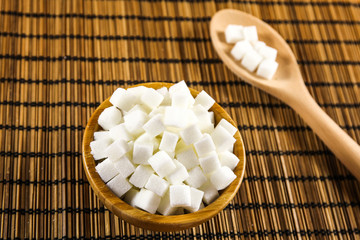 Sugar Cubes in Bowl and on Wooden Spoon over Wooden Background