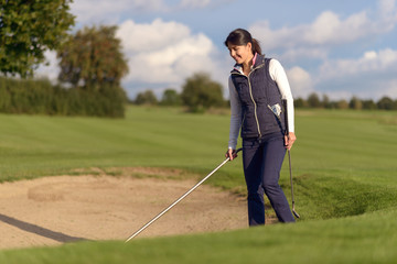 Frau harkt einen Bunker auf dem Golfplatz