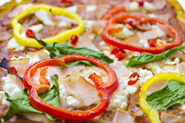 Pizza toppings. Oven baked pizza topped with halloumi, cottage, mozzarella cheese, spinach, turkey, ham, red and yellow peppers, chili, basil and tomato sauce with selective focus on pepper.