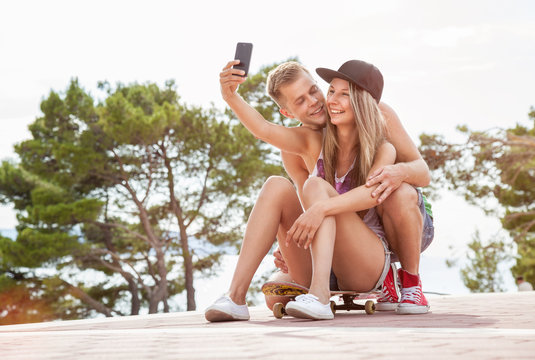 Happy couple with sitting on skateboard and taking a selfie