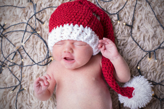 New born baby in a Santa hat surrounded by fairy lights. 