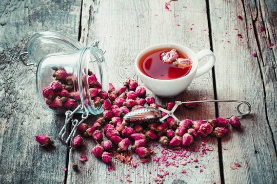 Dry rose buds, tea cup, strainer and glass jar with rosebuds. Se