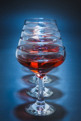 Row of aligned stemmed glasses filled with red wine over blue background. Shallow depth of field.