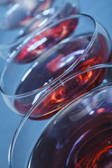 Aligned wine glasses bowls filled with red wine over blue background. Very shallow depth of field.