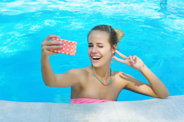 Adorable young woman having fun in the swimming pool and taking photo of herself winking