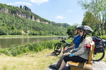 Happy adult couple cyclists sitting on a bench and admiring the
