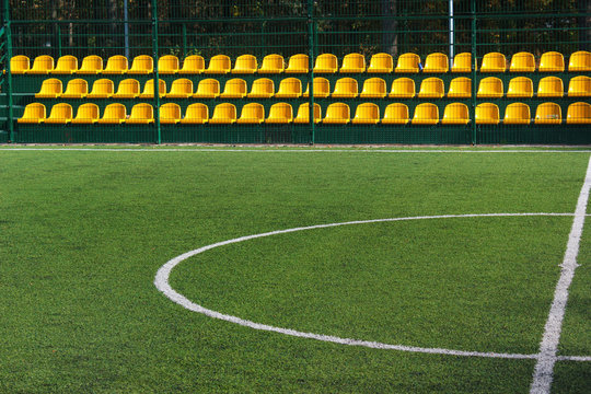 Green grass and yellow seats at empty mini soccer stadium