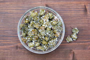 Salted capers in bowl on wooden table seen from above