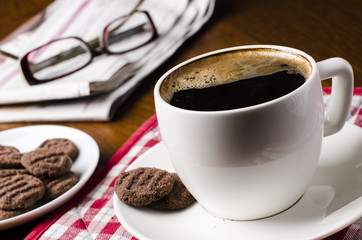 Breakfast on a wooden table consist of coffee, biscuit with news and glasses