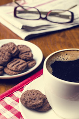 Cup of coffee with biscuit, newspaper and glasses on a wooden table