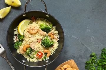 Photo sur Plexiglas Plats de repas Couscous dish with chicken, broccoli, tomato, cashew nuts. Lemon, cashew nuts and parsley on the side, photographed overhead on slate with natural light.
