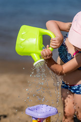 little girl pours water on the water mill on the beach, summer