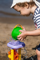 little boy pours water on the water mill on the beach, summer