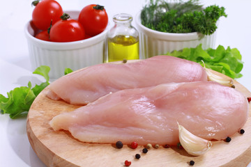 Raw chicken breast fillets decorated with salad, olive oil and cherry tomatoes on wooden cutting board. Diet food, healthy lifestyle
