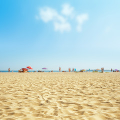 sand on the beach with blurred sea and peoples, sky with clouds