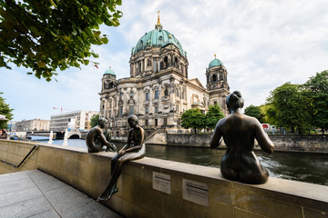 3 statues sit at the riverside. In the background is the Berliner Dom.