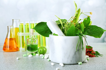 Herbs in mortar, test tubes and pills,  on table, on light background