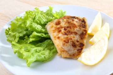 Dish of fish fillet with lettuce and lemon on table close up