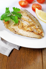 Dish of fish fillet with parsley and tomato on table close up