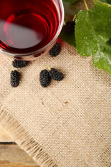 Glass of refreshing mulberry juice with berries on table close up