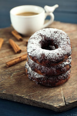 Delicious doughnuts with chocolate icing and cup of coffee on table close up