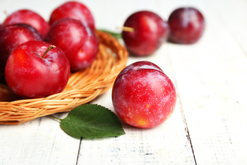 Ripe plums in wicker tray on wooden table, closeup
