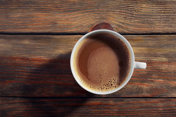 Cup of coffee with foam on wooden table, top view