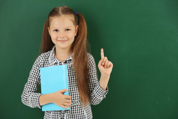 Beautiful little girl with book,  on blackboard background