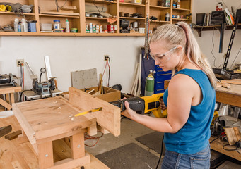 Young adult female woodworker sawing wood plank with reciprocating electric saw.