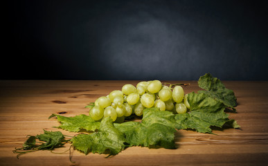 Bunch of green grapes and leaves against brown wooden table