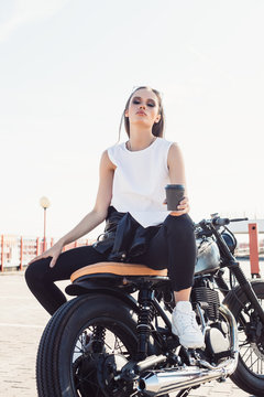 girl with cup of coffee sitting on vintage custom motorcycle