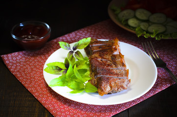 Grilled beef steak with salad and sauce on wooden table at white plate. Salad with tomatoes and cucumbers and sauce barbecue. Leafs of basil as decoration.