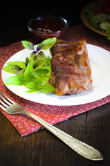 Grilled beef steak with salad and sauce on wooden table at white plate. Salad with tomatoes and cucumbers and sauce barbecue. Leafs of basil as decoration.