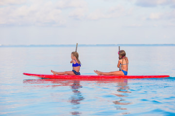 Little cute girls swimming on surfboard during summer vacation