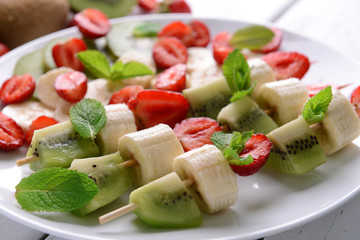 Fresh fruits on skewers in plate on table, closeup