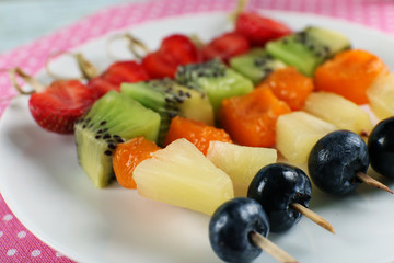 Fresh fruits on skewers in plate on napkin, closeup