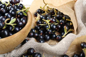Ripe black currants in wooden bowl on sackcloth, closeup
