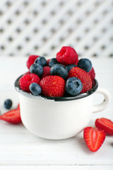 Tasty ripe berries in cup on wooden table close up