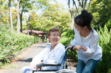 公園の中 車椅子の高齢者と介護する女性