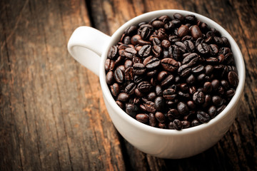 Coffee beans in white cup put on old wooden table.