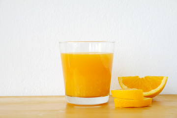 Glass of orange juice with sliced orange on wooden table