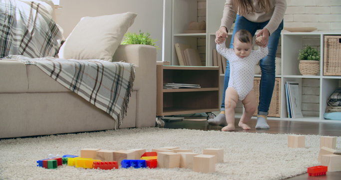 Young mother teaching her adorable baby son to walk and play with toy blocks