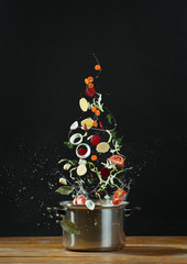 Fresh vegetables falling into a stainless steel casserole 