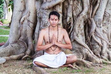 A young brahmin sits in meditation under a banyan tree in India 
