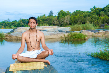 Fototapeta premium A young brahmin sits in meditation on a river bank in India 