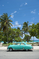Classic vintage American car stands parked in front of palm trees on the road next to the beach