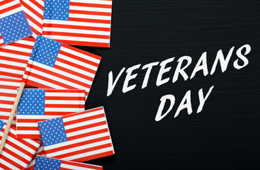 The phrase Veterans Day in white text on a blackboard alongside paper flags of the United States of America