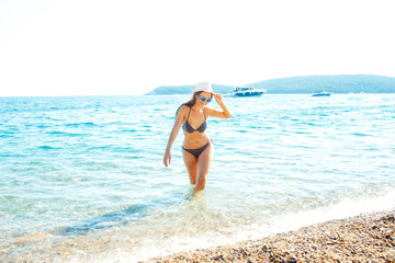 Woman in sun hat and bikini standing with her arm raised to her